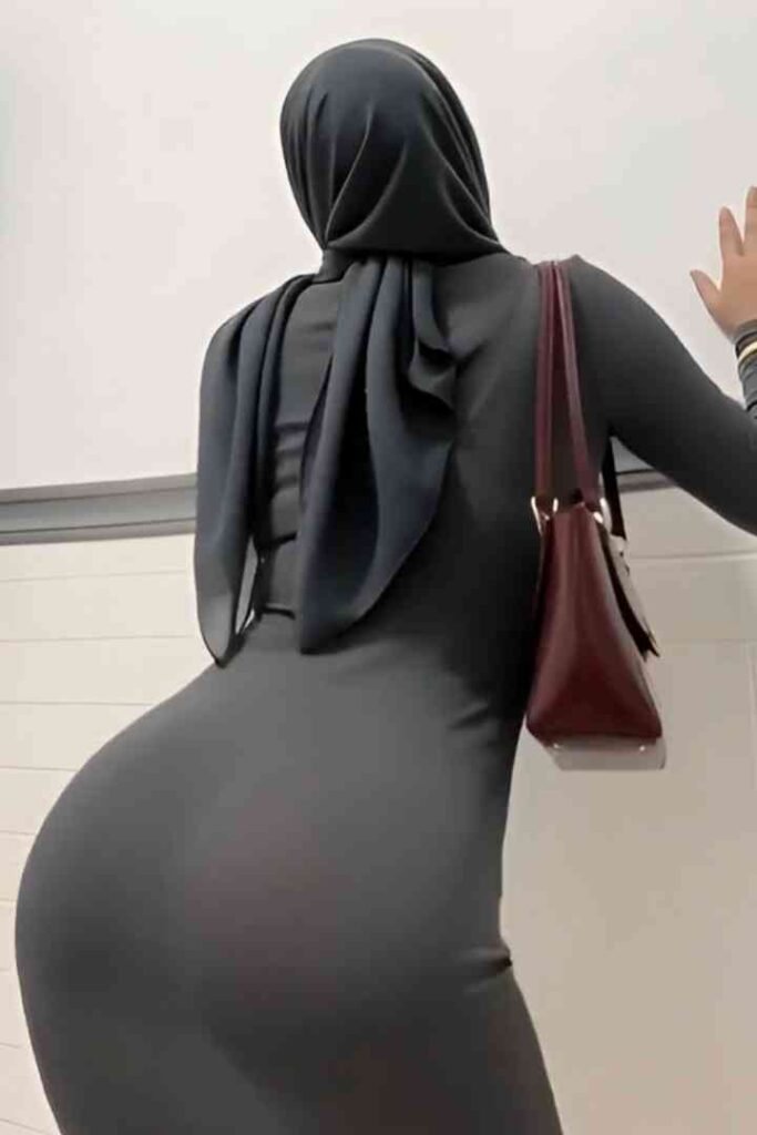 Woman in grey hijab and dress with a maroon handbag.