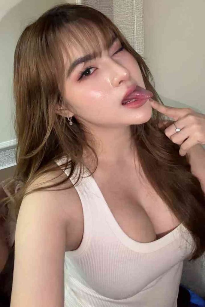 Young woman with brown hair and bangs, winking and sticking out her tongue.